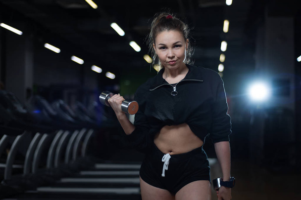 Fitness girl posing in the gym with dumbbells in her hands, showing off her body - Valokuva, kuva
