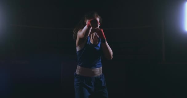 Mirando a la cámara, una hermosa boxeadora golpea contra un fondo oscuro con una luz retroiluminada. Steadicam tiro
 - Metraje, vídeo