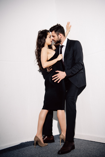 attractive brunette woman kissing with handsome man near white wall  - Foto, immagini