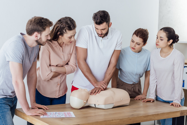 group of people looking at man performing cpr on dummy during first aid training - Photo, Image