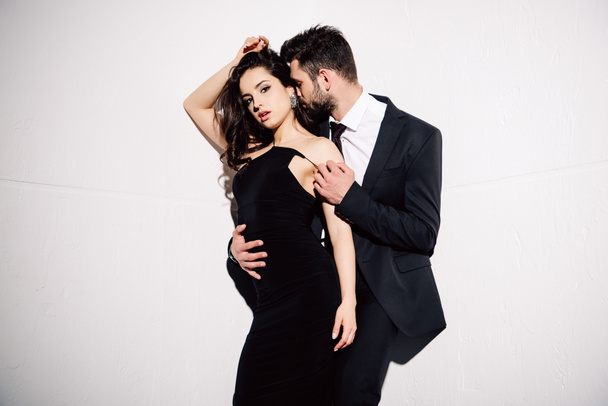 брюнетка жінка в чорній сукні, що стоїть з чоловіком на білому
 - Фото, зображення