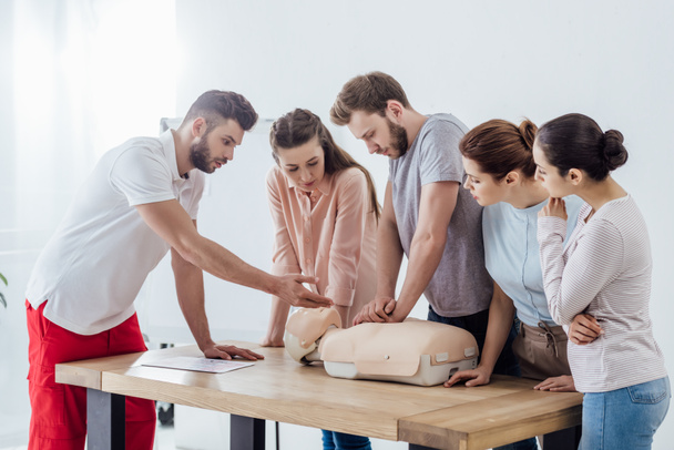 group of people with handsome instructor performing cpr on dummy during first aid training - Foto, Imagem