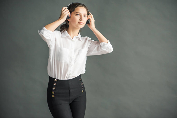 young pretty girl with blond hair with a nice smile, dressed in a white shirt holds headphones for music with her hands near the ears  - Фото, изображение
