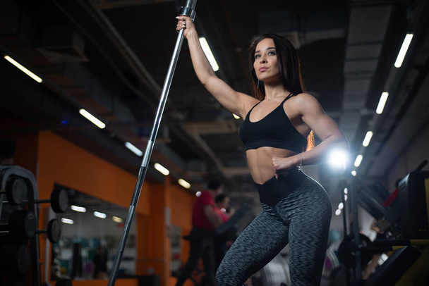 Girl posing in the gym, showing off her body, holding a barbell - Foto, Bild