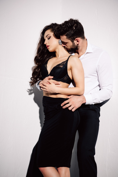 handsome man kissing neck of beautiful woman in black dress on white  - Foto, imagen