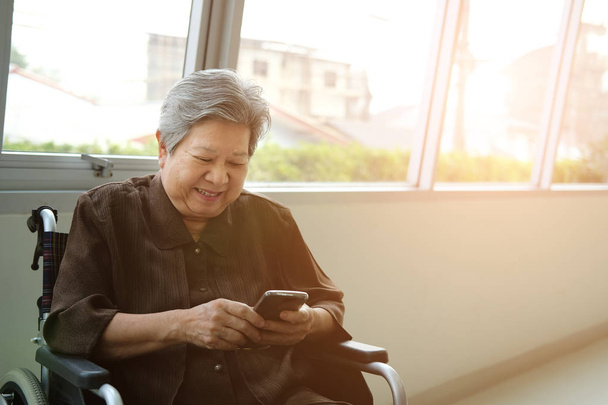idősebb nő kerekesszékkel gazdaságban mobiltelefon. idős magas rangú u - Fotó, kép