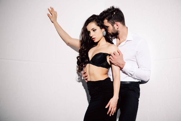handsome man undressing beautiful woman in black lace bra on white  - 写真・画像
