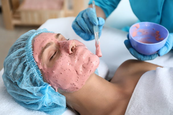 Schoonheidsspecialist alginaat-masker toe te passen op jonge vrouw gezicht in de beauty salon - Foto, afbeelding