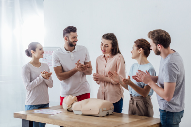 group of smiling people with cpr dummy applauding during first aid training class - Фото, изображение