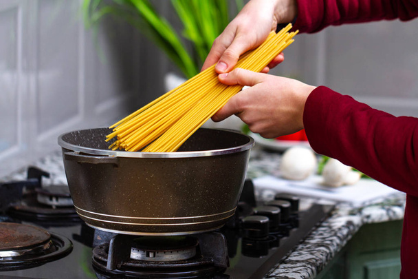 Housewife is cooking spaghetti in a saucepan for a lunch at home.  - 写真・画像