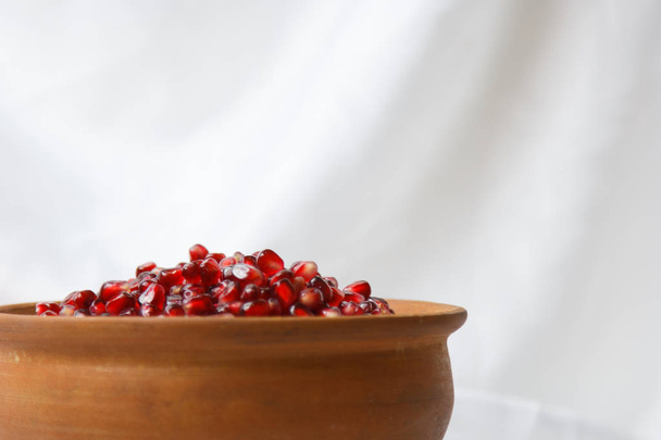 whole ripe pomegranate, pomegranate grains in a brown ceramic plate on a white fabric background, close up - Photo, Image