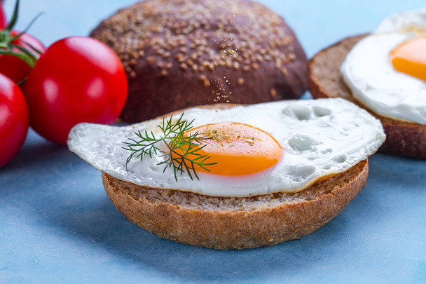 Buns with homemade, fried chicken eggs sprinkled with spices and salt for a breakfast on a blue background. Protein food. Eggs sandwiches - Fotoğraf, Görsel