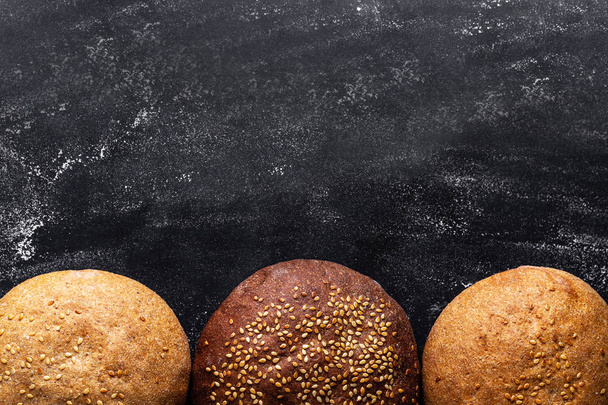 Yellow and brown sesame buns on a black background. Top view. Flour and bakery products. Fresh bread. Copy space  - Foto, immagini