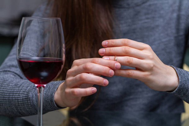 Divorced woman pulling wedding ring from finger and drinking a glass of a red wine because of adultery, betrayal and a failed marriage. Divorce concept. Relationship and love end. Life problems  - Photo, Image