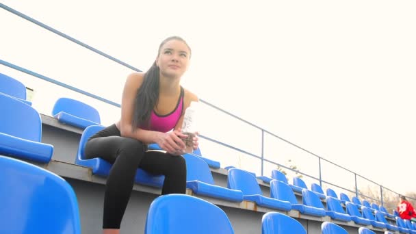 Mladý sportovec asijské dívka odpočívá, sedí na stadionu za slunečného dne. - Záběry, video