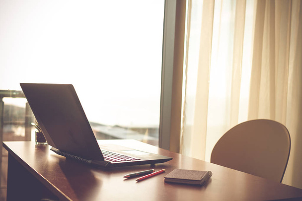 Online praca w domu przy użyciu laptopa. Przytulne miejsce pracy w pobliżu okna o zachodzie słońca  - Zdjęcie, obraz