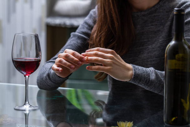 Divorced woman pulling wedding ring from finger and drinking a glass of a red wine because of adultery, betrayal and a failed marriage. Divorce concept. Relationship and love end. Life problems  - Photo, Image
