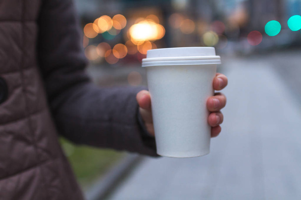 Młoda kobieta w dorywczo ubrania trzyma filiżankę kawy papieru i korzystających spacer w mieście wieczorem. Kawa z dala i iść  - Zdjęcie, obraz