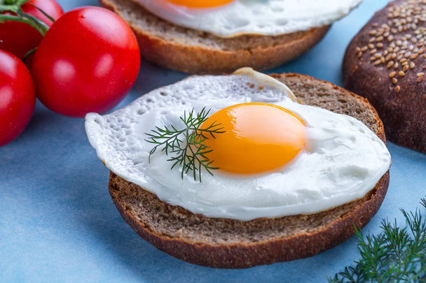 Buns with homemade, fried chicken eggs for a healthy breakfast on a blue background. Protein food. Eggs sandwiches  - Fotoğraf, Görsel