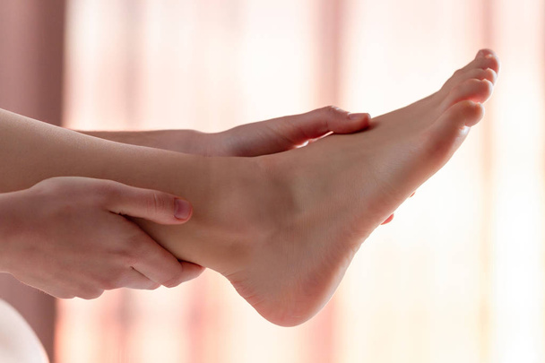 Young woman doing a relaxing foot massage at home on the bed after a long, hard working day. Manual therapy. Treatment pain, fatigue and discomfort legs - Foto, afbeelding