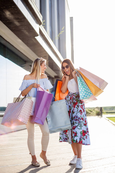 Két fiatal nő, könyv bevásárló táskák, előtt egy bevásárlóközpontban - Fotó, kép
