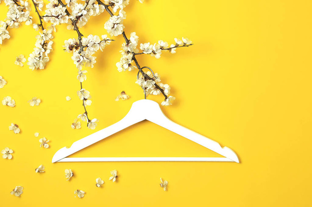 黄色の背景に春の開花枝に掛かっている白い木製ハンガー。春販売コンセプト ディス カウント ストア ショッピング空ハンガー。創造的なファッションの美しさのバナーです。フラット レイアウト平面図コピー スペース. - 写真・画像