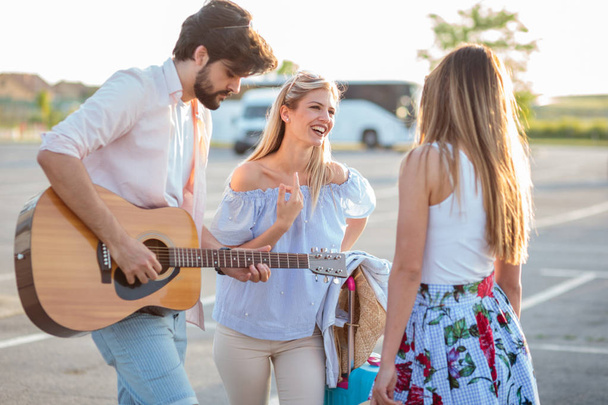 Gruppo di giovani turisti divertirsi e suonare la chitarra in un parcheggio, in attesa di trasporto
 - Foto, immagini