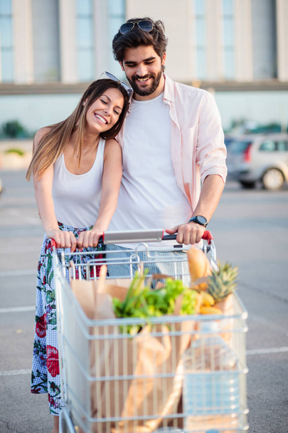 Happy young couple with full shopping cart in front of the mall - Foto, Bild