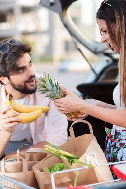 Playful young couple loading grocery bags into a car - Photo, image