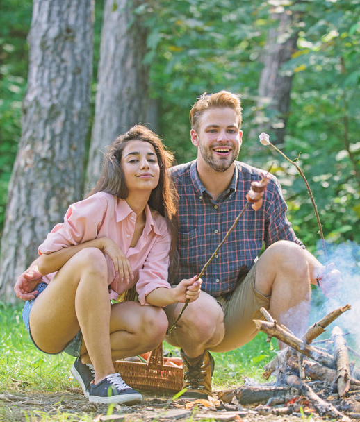 Couple roasting sausages on sticks nature background. Couple in love enjoy camping forest roasting sausage at bonfire. Traditional roasted food as attribute of picnic. Camping and picnic - Photo, Image