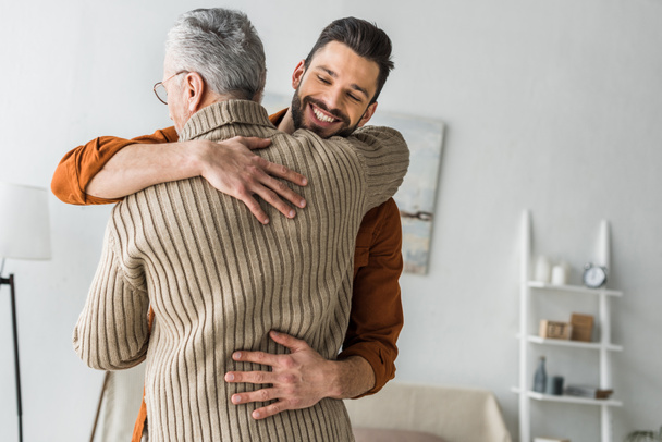 happy bearded man smiling while hugging elder father at home  - Foto, Imagen