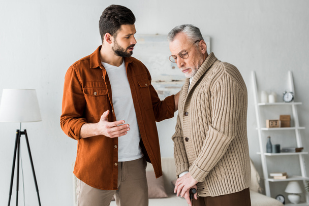 handsome bearded man gesturing while looking at sad senior father  - Photo, Image