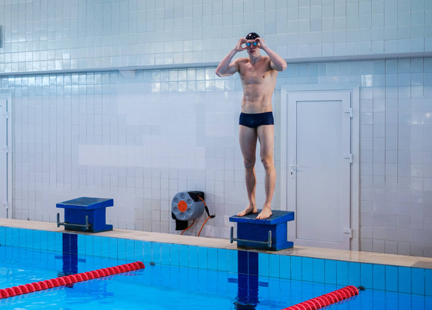 Nadador muscular preparándose para saltar desde el bloque de salida en una piscina
 - Foto, imagen
