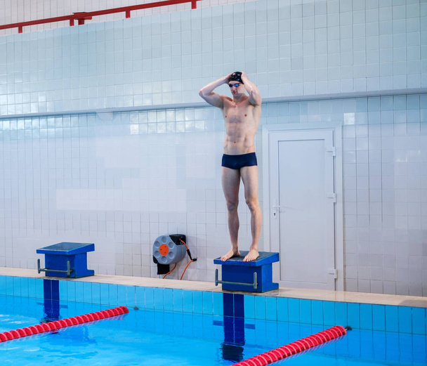 Muskelschwimmer bereitet sich auf Sprung aus dem Startblock im Schwimmbad vor - Foto, Bild