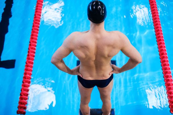 Мышечный пловец готовится к прыжку из стартового блока в бассейн
 - Фото, изображение