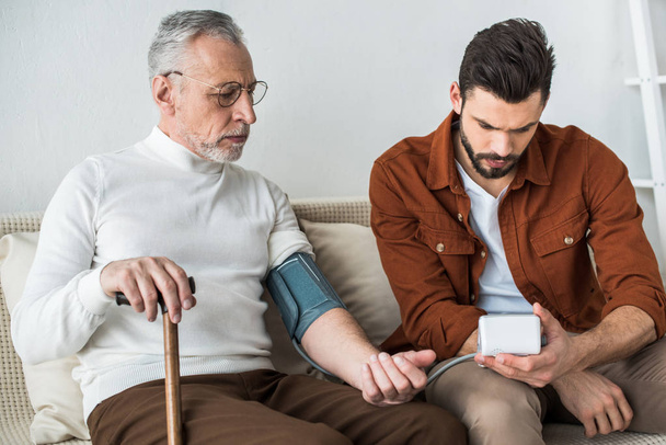 uomo barbuto misurare la pressione sanguigna del padre anziano in occhiali
 - Foto, immagini
