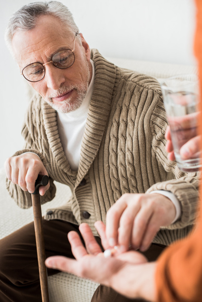 szelektív összpontosít nyugdíjas Atya fiának, gazdaság pohár vizet kézzel tablettát  - Fotó, kép