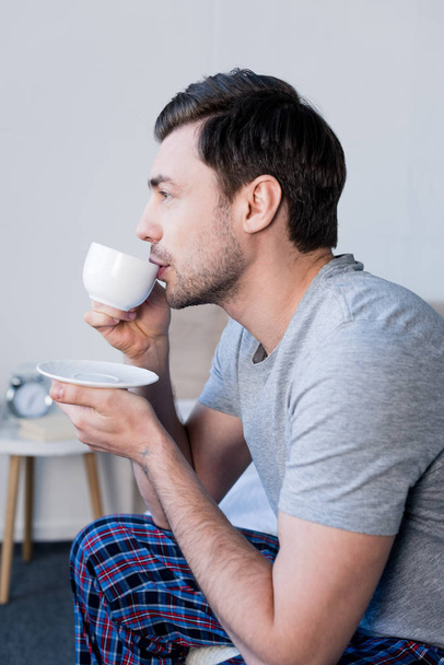 pensive handsome man drinking morning coffee in bedroom at home - Foto, immagini