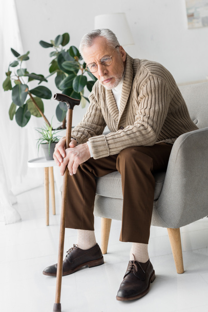 triest senior man in glazen zitten in fauteuil thuis  - Foto, afbeelding