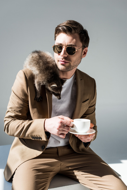handsome man holding coffee cup, with cute raccoon on shoulder - Foto, Imagem