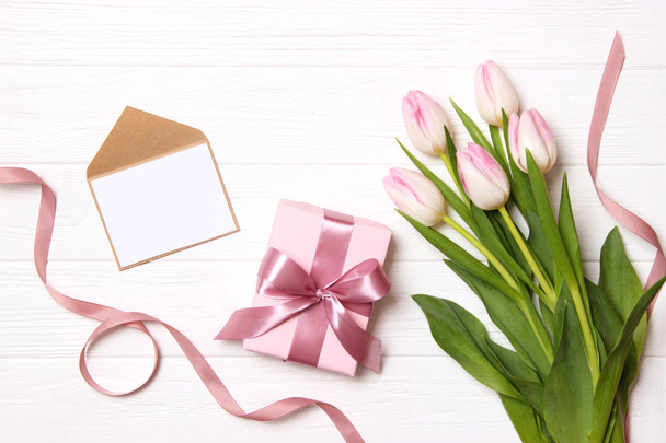 Ein Strauß schöner Tulpen und ein Geschenk auf einem hölzernen Hintergrund von oben. Hintergrund Muttertag, Internationaler Frauentag. Urlaub, beschenke. - Foto, Bild
