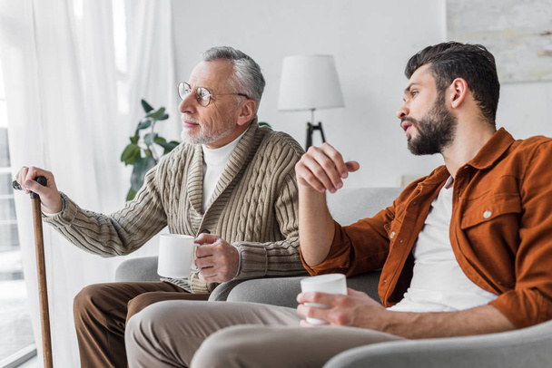 senior father in glasses sitting with handsome man and holding cup  - Photo, Image