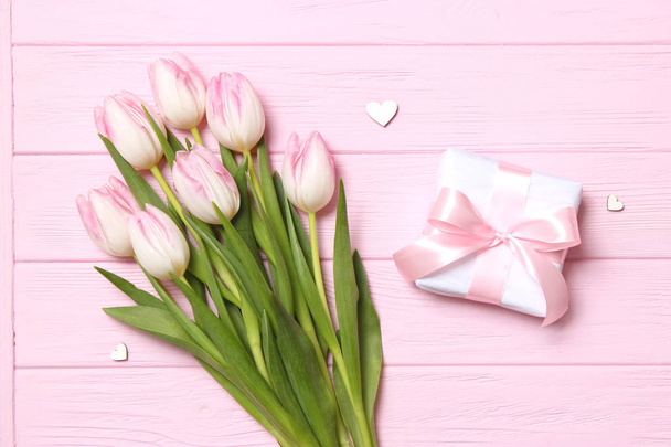 Een boeket van prachtige tulpen en een geschenk op een houten achtergrond bovenaanzicht. Achtergrond moederdag, Internationale Vrouwendag. Vakantie, geef een geschenk.. - Foto, afbeelding