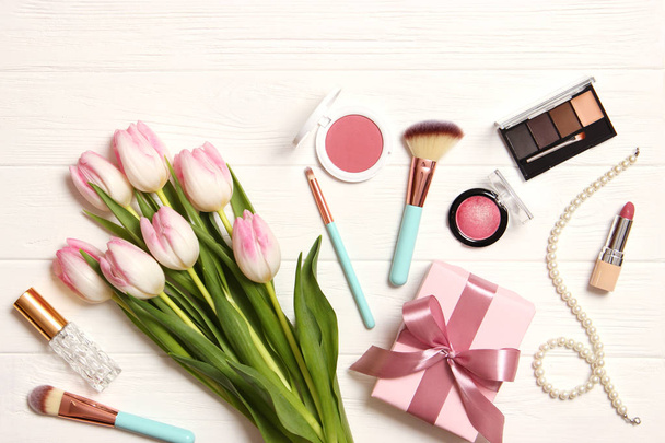 makeup products and beautiful spring flowers on wooden background. Top view. - Fotó, kép