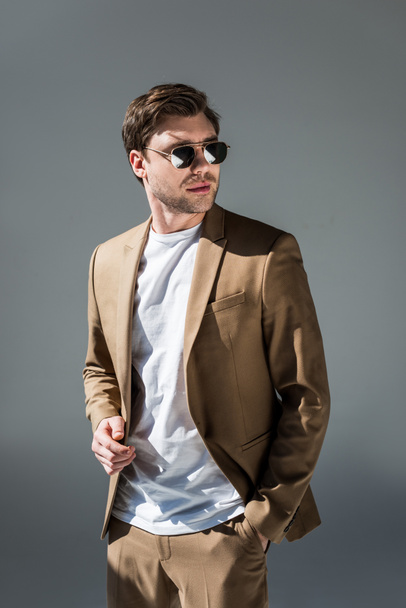 handsome man in beige suite with hand in pocket looking away on grey - Photo, Image