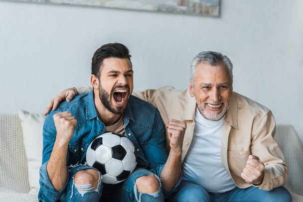šťastný starší muž sleduje mistrovství a fandění s pohledný syn drží fotbal  - Fotografie, Obrázek