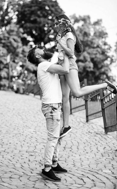 Guy raising up girlfriend. Romantic date walk. Happy to see her. Man carrying girlfriend in hands while she holds flower bouquet on l romantic date. Couple in love meeting for date park background - Фото, зображення