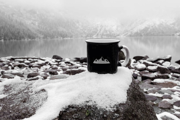 cup for the inscription. black mug on the background of a mountain lake in winter - Photo, Image