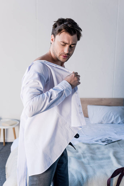 handsome sleepy man dressing white shirt in bedroom at home - 写真・画像