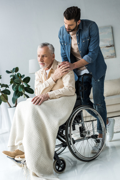 handsome bearded son holding hands with disabled senior father in wheelchair at home  - Foto, imagen